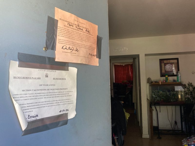 Months-old city notices are hung on the door of a renter's apartment, indicating the home failed city inspection and jeopardizing the landlord’s license to rent.